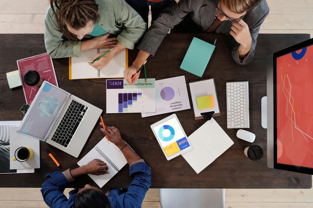 Personnes collaborant autour d'une table avec ordinateurs, graphiques et notes.