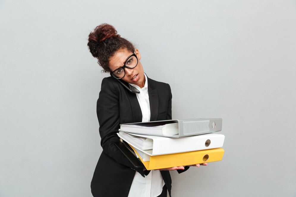 Femme portant des classeurs, parlant au téléphone, air débordé.